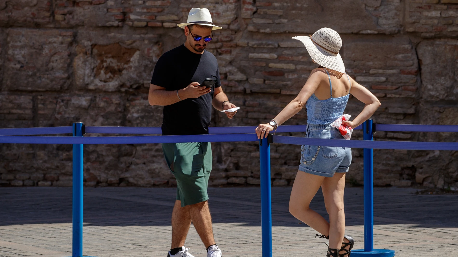 Unos turistas se protegen del sol con sombreros junto al muro de los Reales Alcázares de Sevilla