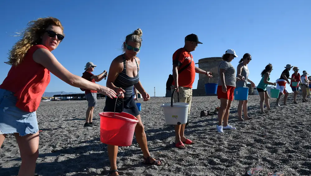 Varios voluntarios llevan este sábado agua de mar a Las Salinas del Cabo de Gata en la playa de La Fabriquilla (Almería). EFE/ Carlos Barba
