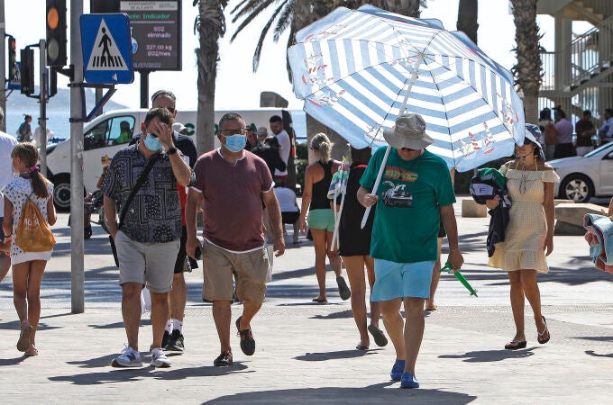 Un hombre se protege del intenso calor con una sombrilla de playa por las calles de la ciudad de Alicante.