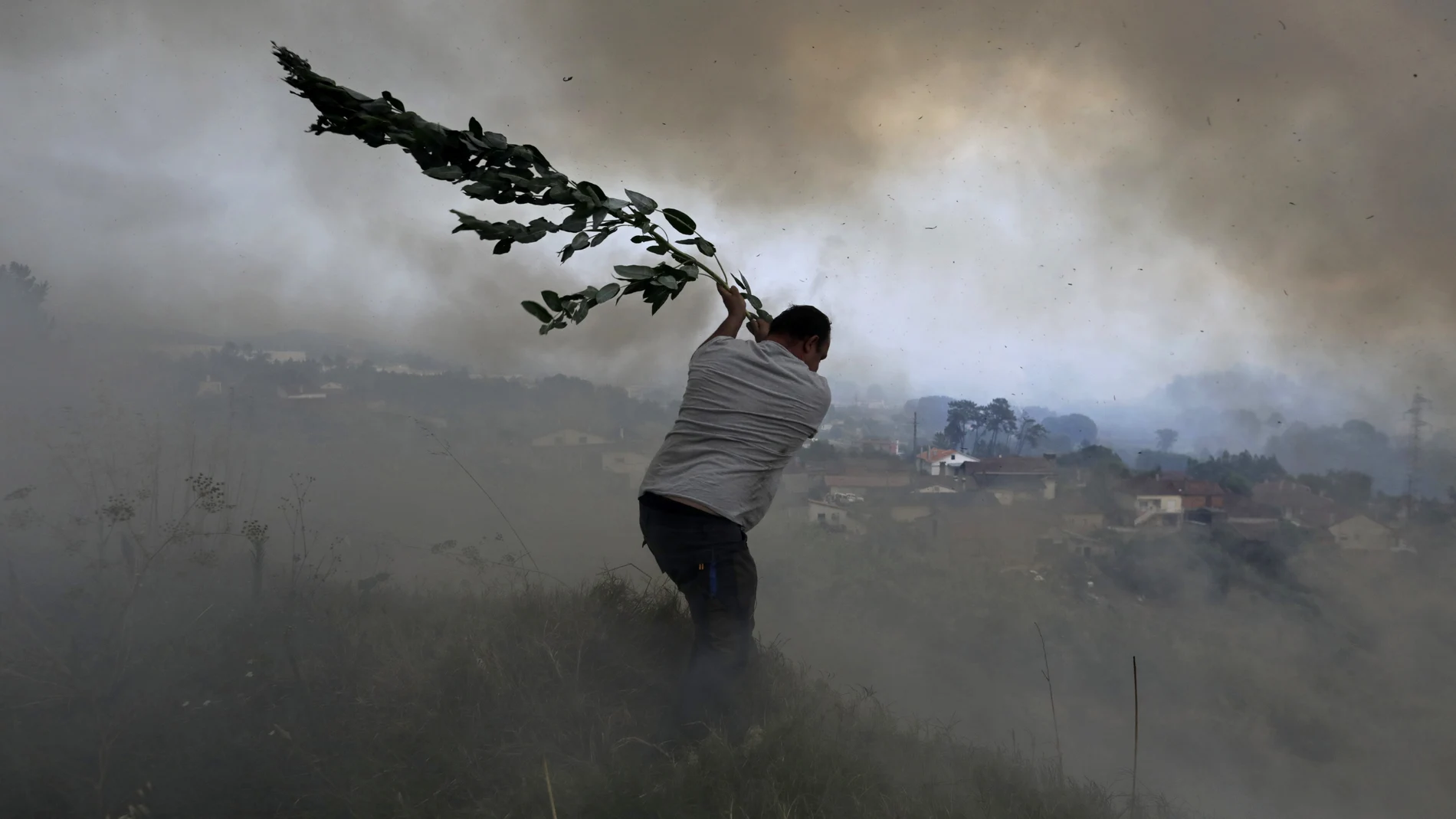 Un voluntario utiliza una rama de árbol tratando de evitar que un incendio forestal llegue a las casas en Casal da Quinta, a las afueras de Leiria, en el centro de Portugal