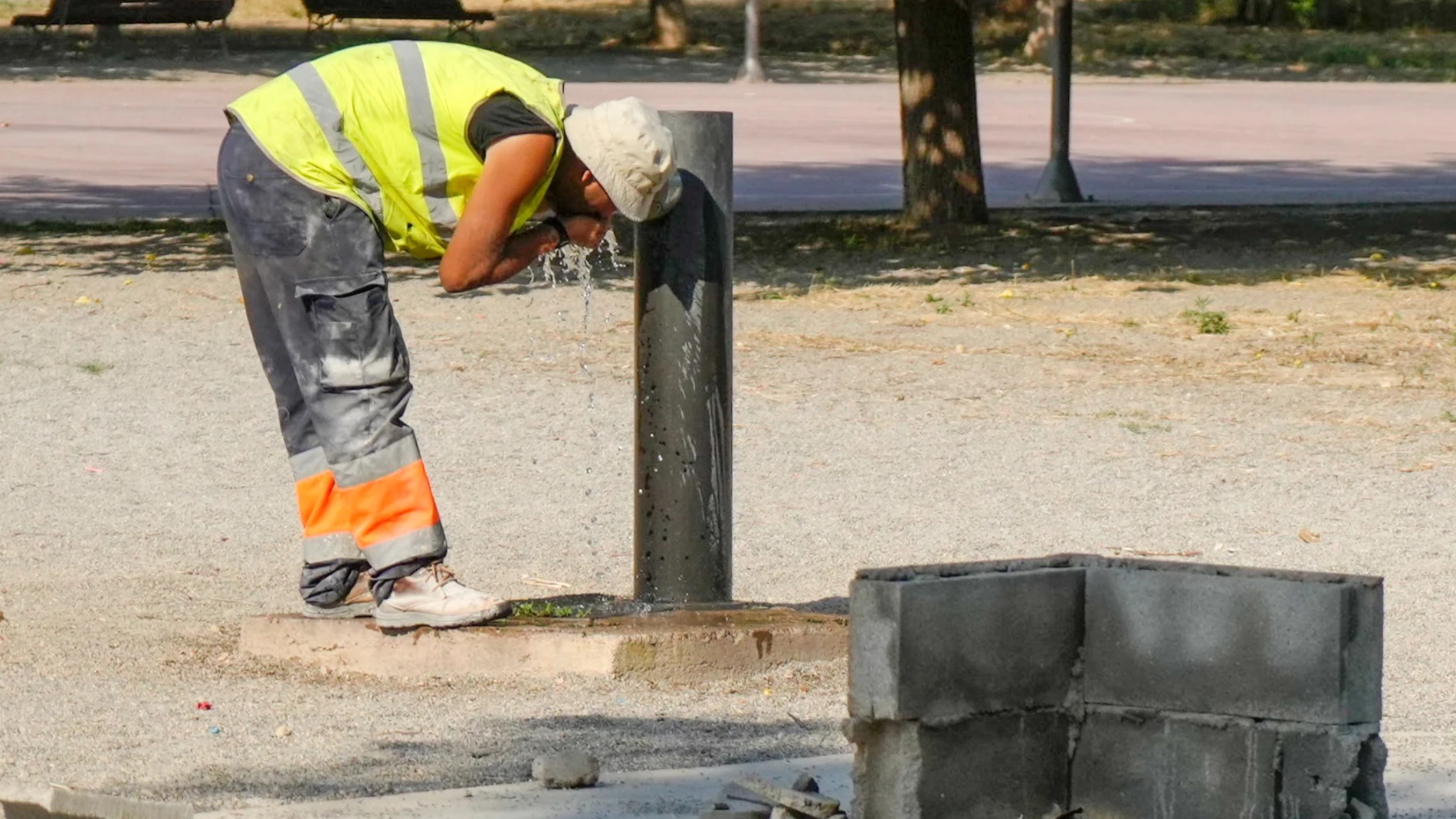 Un trabajador se refresca en un fuente de un parque de Lleida