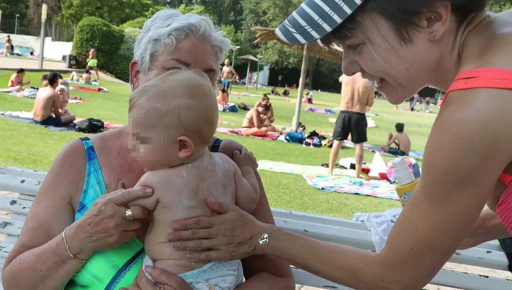 Una madre aplica crema solar a su bebé en una piscina de Palencia