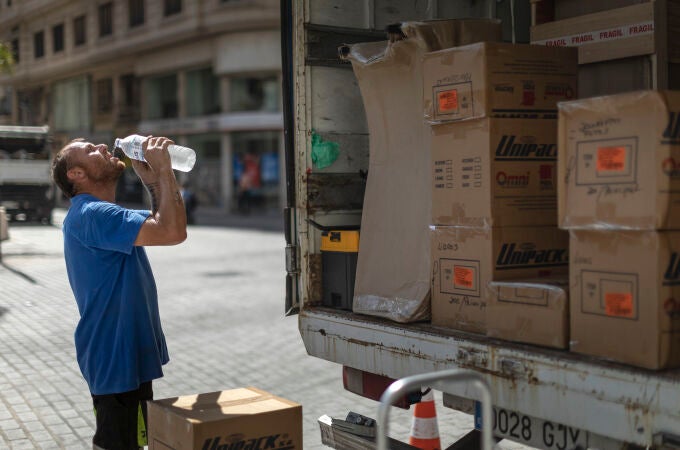 Un trabajador de una empresa de mudanzas bebe agua para combatir el calor en una calle del centro de Valencia