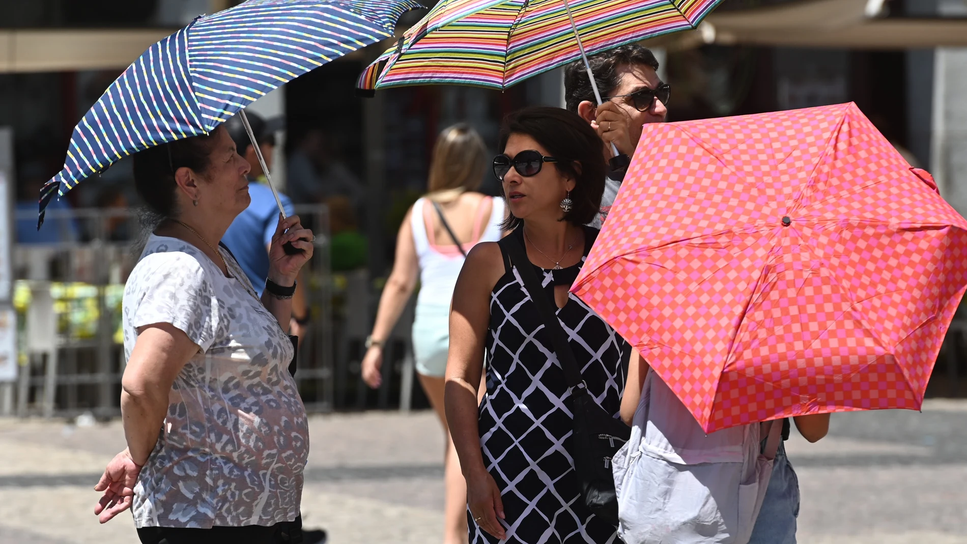 Varias personas pasean con una sombrilla por el centro de Madrid.