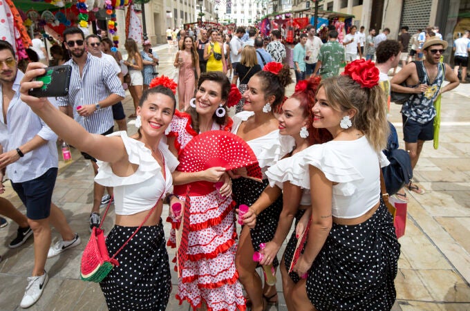 Un grupo de mujeres vestidas de flamencas se fotografía en la calle Larios del centro histórico de la ciudad malagueña, donde se celebra parte de la Feria de Málaga, que ha empezado hoy sábado. EFE/ Daniel Pérez
