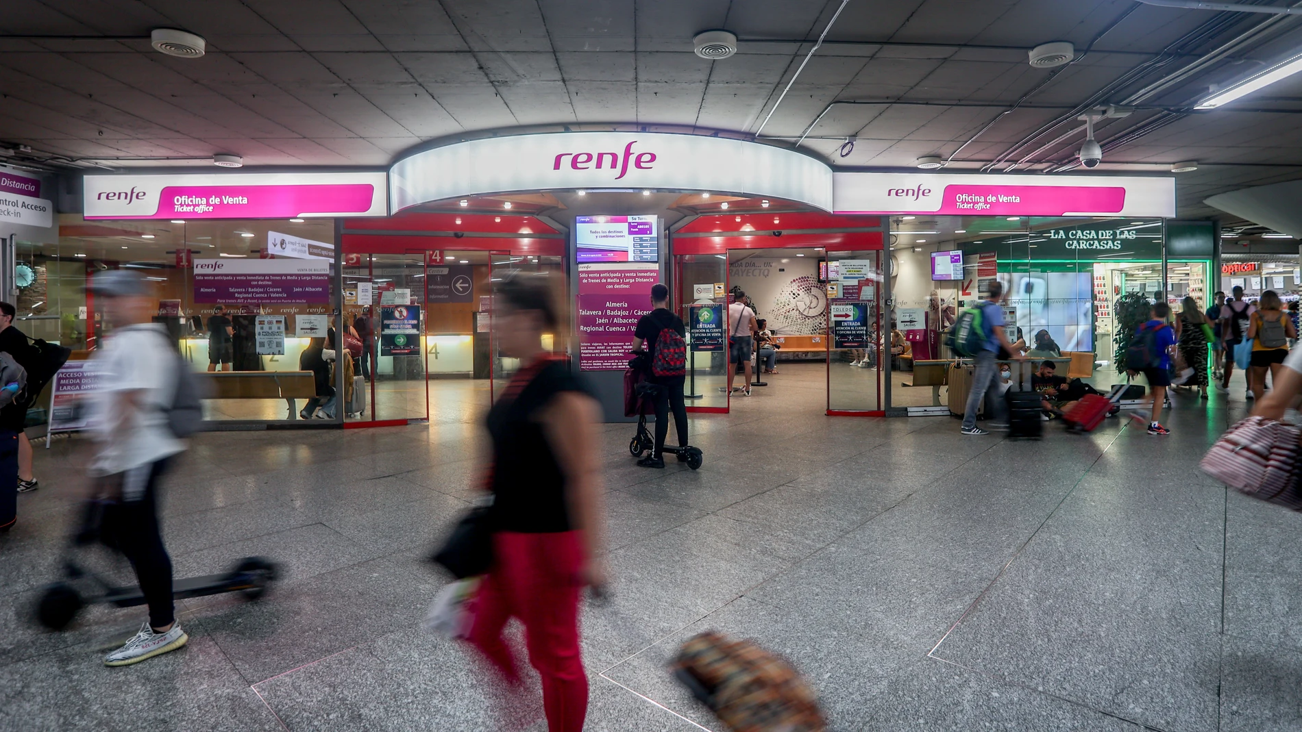 Viajeros pasan por delante de la oficina de Renfe, en la estación de Atocha