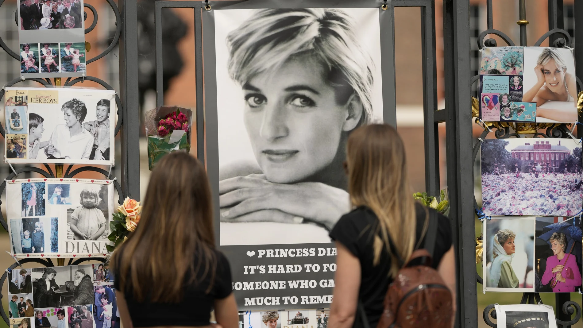 Dos mujeres contemplan los retratos de la princesa Diana en la puerta principal de Kensington. (AP Photo/Alastair Grant)