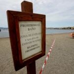 Cartel donde se indica la prohibición del baño debido a las labores de los trabajadores municipales que están realizando trabajos de limpieza en la playa de Poniente por el vertido ocasionado por el buque OS35. Nono Rico/EP