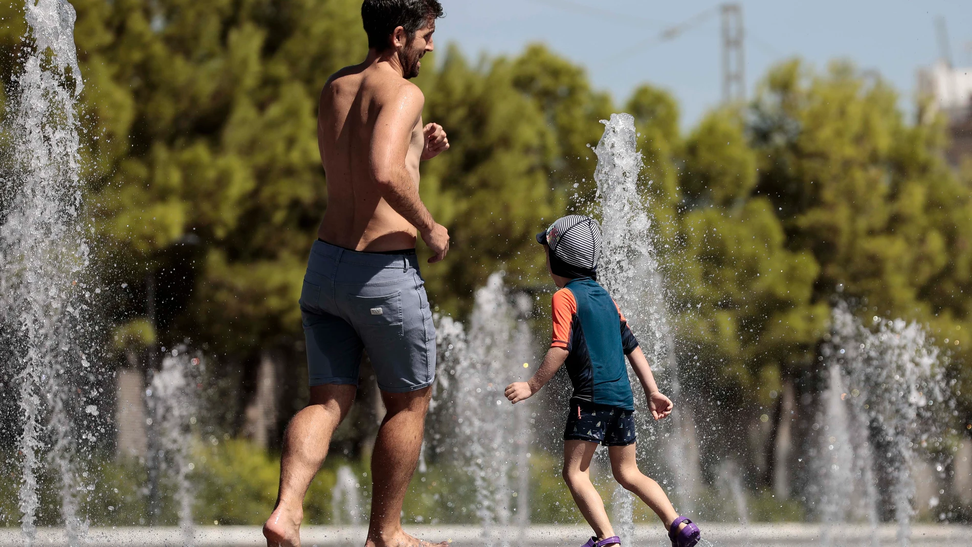 Un niño y su padre se refrescan en una fuente en Valencia
