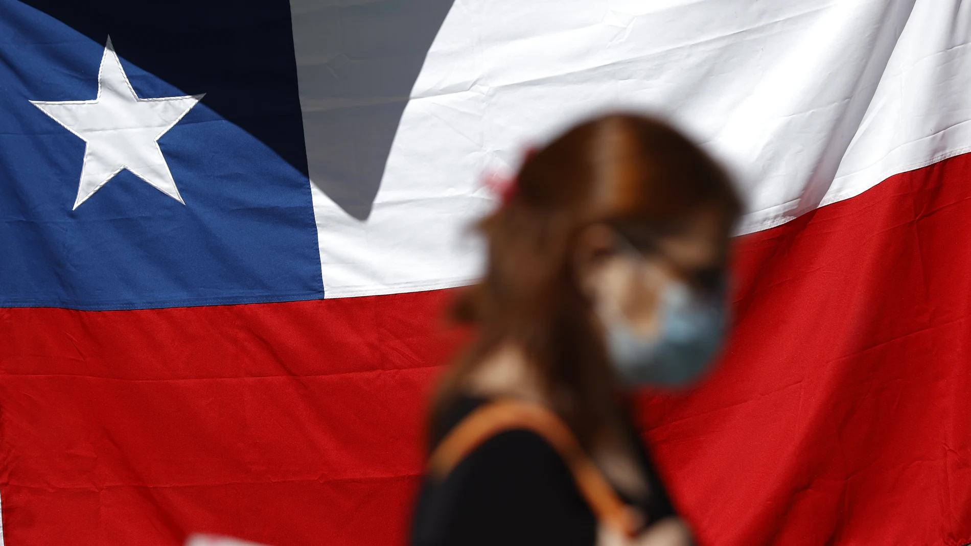 Una mujer camina frente a una bandera de Chile hoy, en Santiago (Chile).
