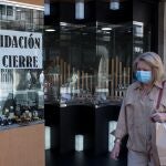 Una mujer pasa ante un comercio con un cartel de "liquidación por cierre" en Orense