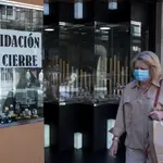Una mujer pasa ante un comercio con un cartel de &quot;liquidación por cierre&quot; en Orense