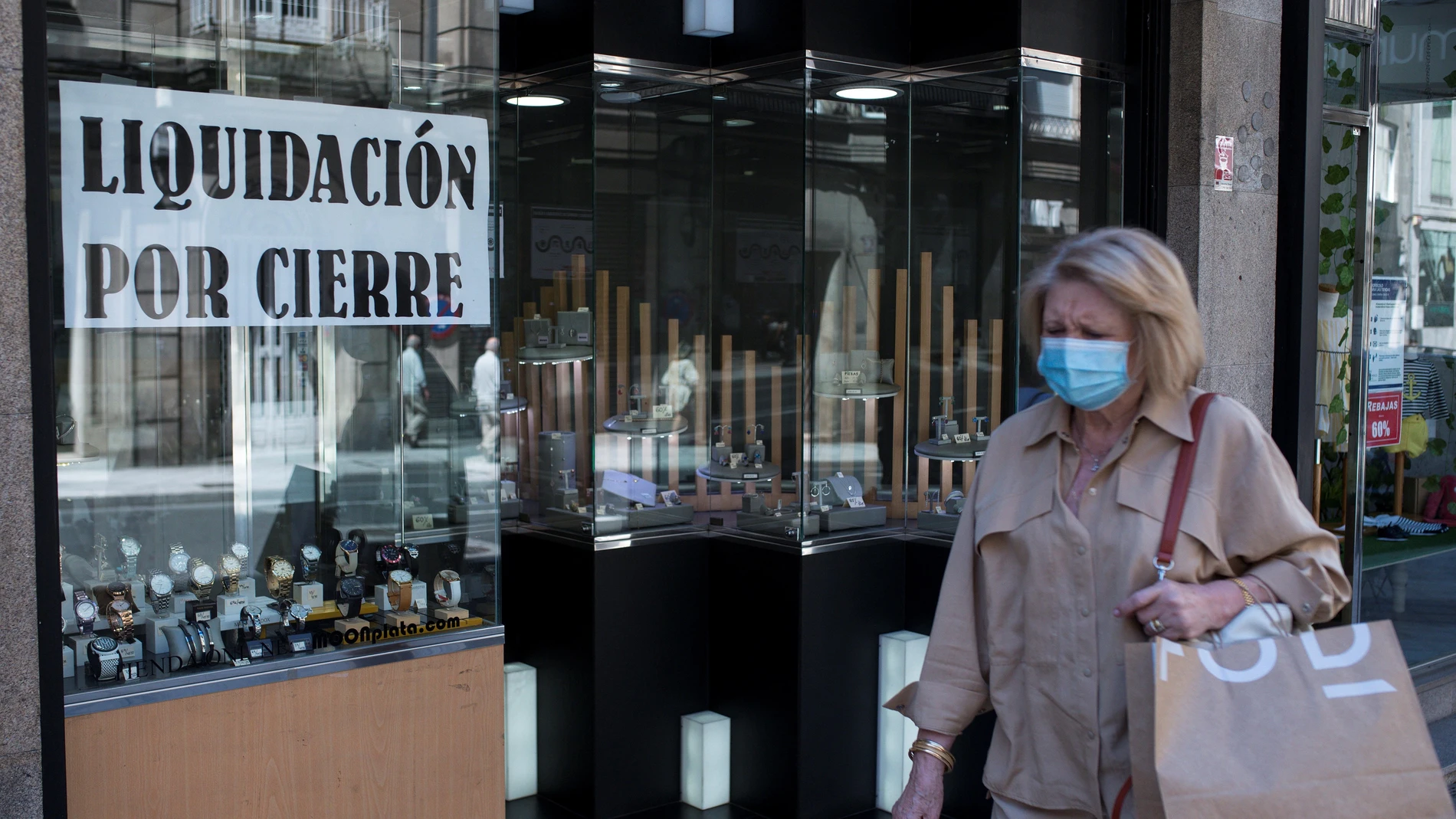 Una mujer pasa ante un comercio con un cartel de "liquidación por cierre" en Orense