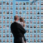 Un hombre sostiene en brazos a una niña frente a un muro con las fotografías de los caídos en la defensa de Ucrania en Kiev