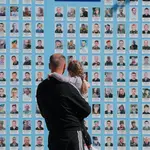Un hombre sostiene en brazos a una niña frente a un muro con las fotografías de los caídos en la defensa de Ucrania en Kiev