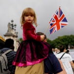 Una niña sujeta una bandera británica mientras numerosas personas se congregan frente al Palacio de Buckingham para rendir tributo a la reina Isabel II