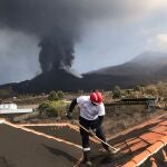 Un hombre limpia de ceniza el tejado de su casa en La Palma
