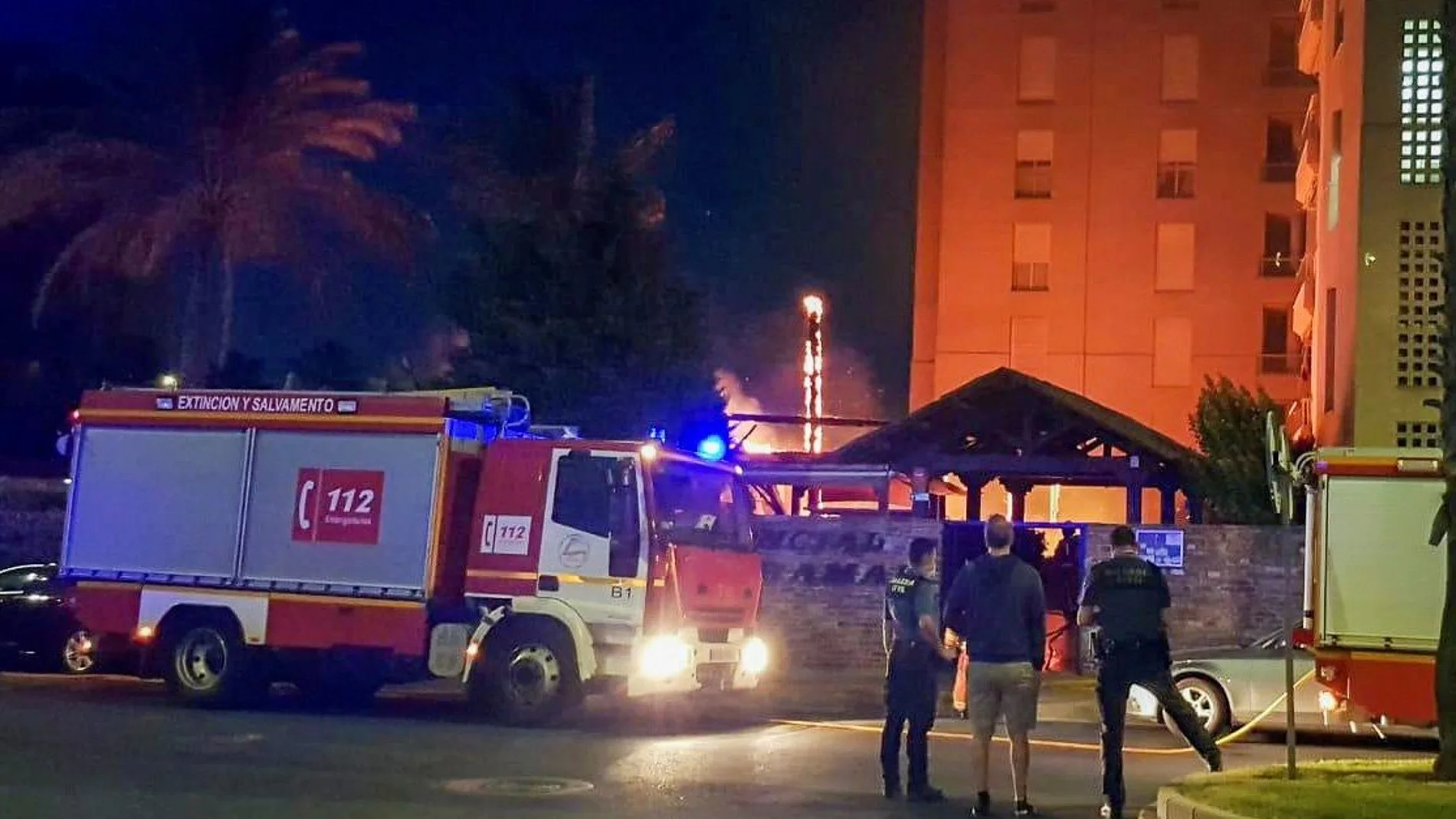 Dos agentes de las fuerzas de seguridad vigilan los alrededores tras prenderse fuego el chiringuito de una piscina de una urbanización