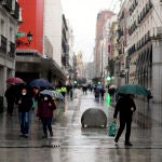 Varias personas caminan protegidas con paraguas ante la lluvia que cae en la capital