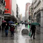 Varias personas caminan protegidas con paraguas ante la lluvia que cae en la capital
