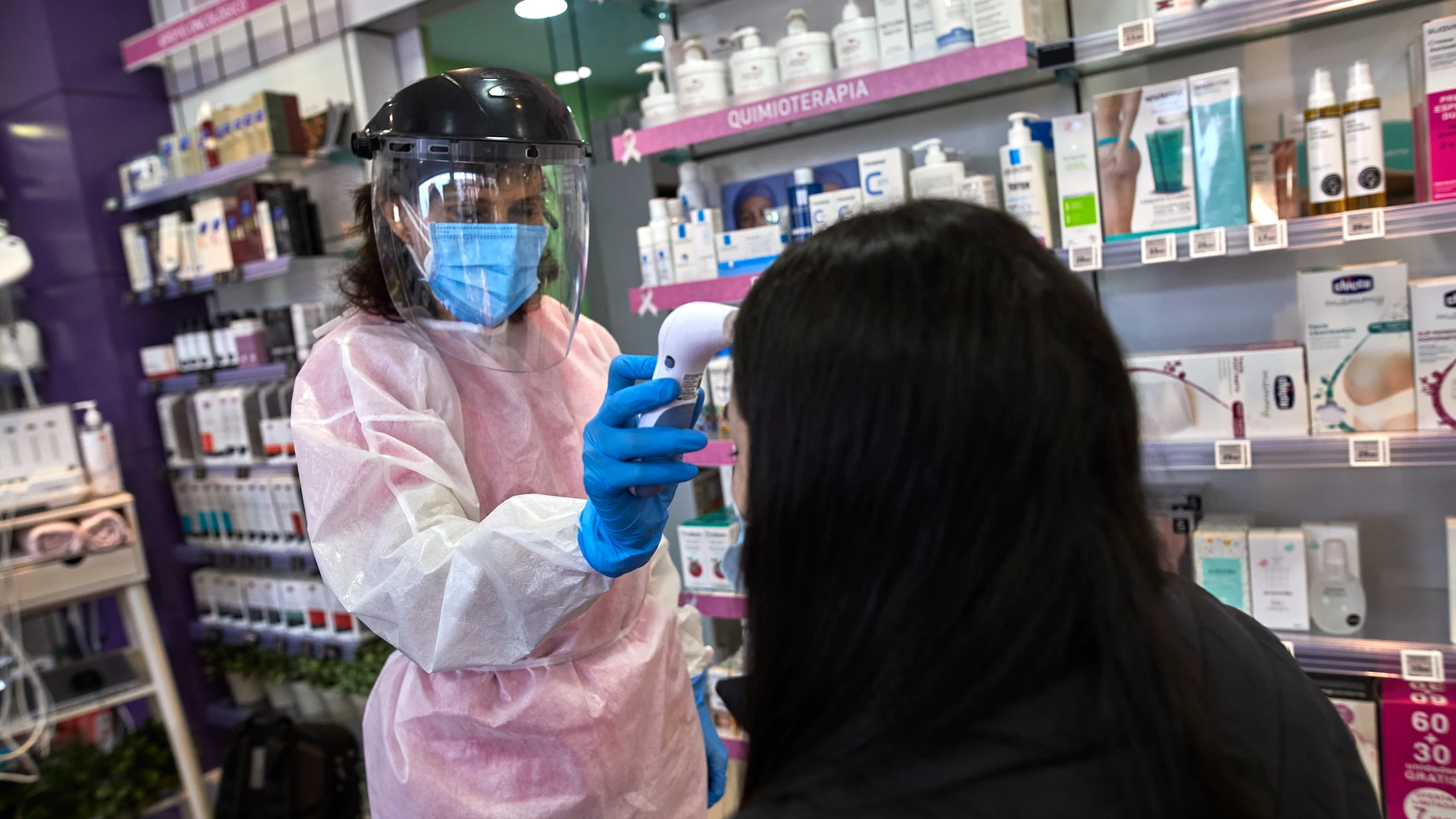 Una farmacéutica madrileña toma la temperatura a una mujer antes de realizarle un test de antígenos