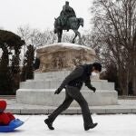 Un hombre tira de un trineo con niños sobre el manto de nieve que cubre el parque del Retiro