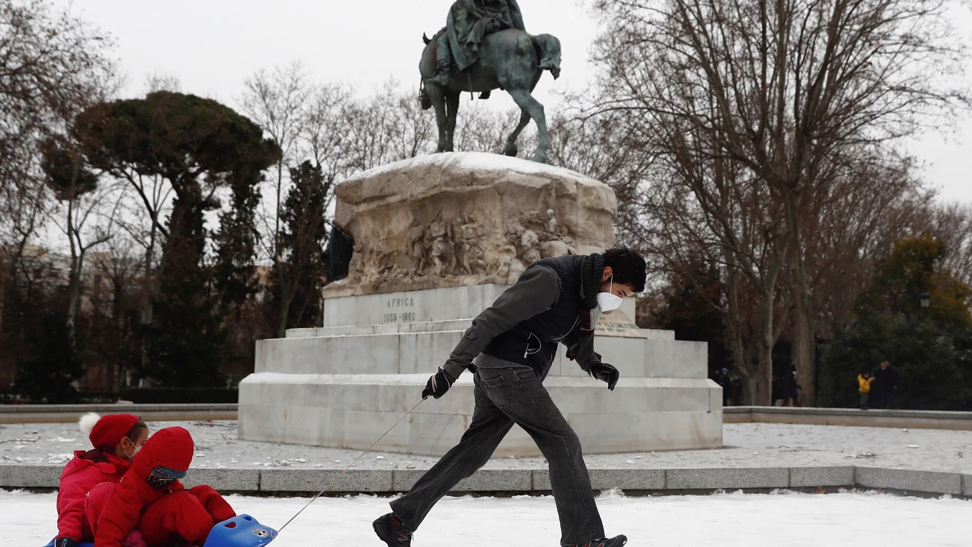 Un hombre tira de un trineo con niños sobre el manto de nieve que cubre el parque del Retiro
