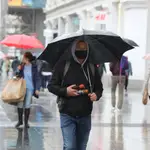 Un vendedor de paraguas camina por el centro de Madrid protegiéndose de la lluvia con uno de ellos