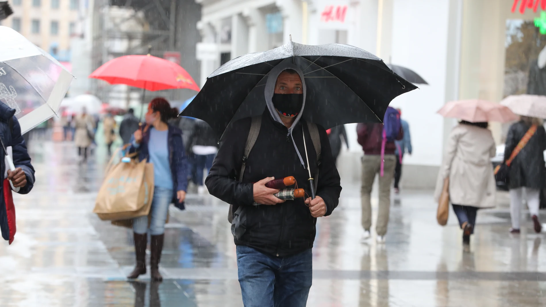 Un vendedor de paraguas camina por el centro de Madrid protegiéndose de la lluvia con uno de ellos