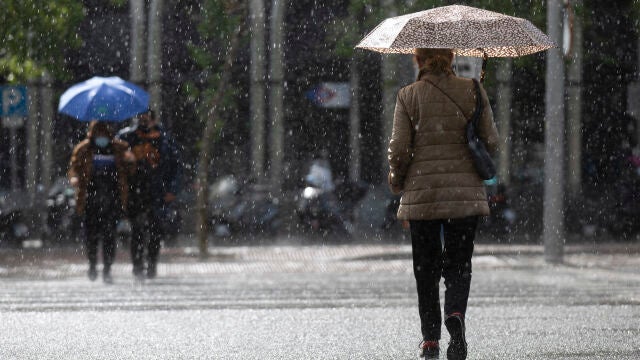 Una mujer bajo la lluvia con su paraguas cruza un paso de peatones en la Castellana de Madrid.