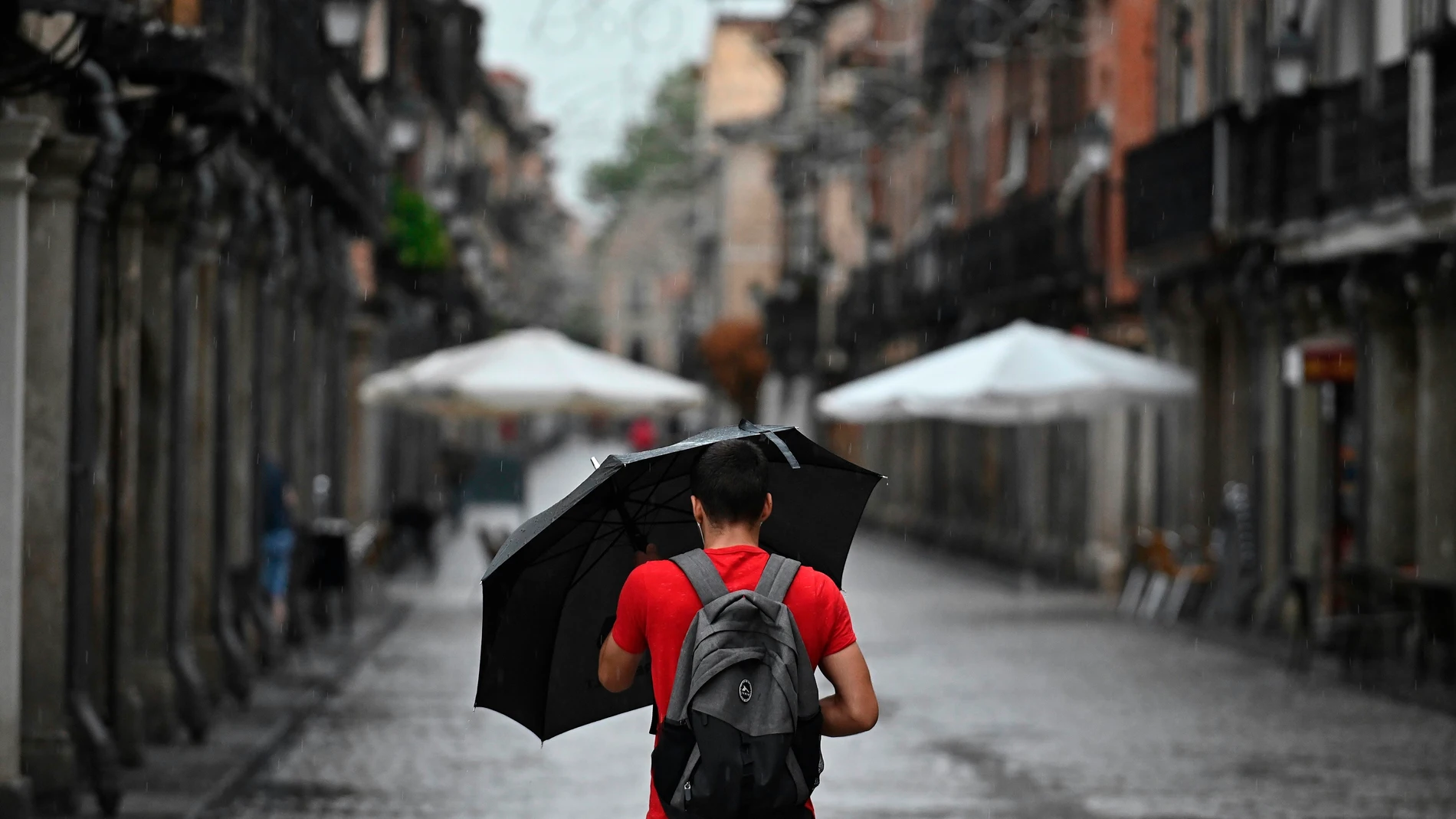 Un hombre se protege de la lluvia que cae en Alcalá de Henares