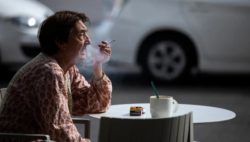 Imagen de una mujer mayor fumando junto a una taza de café en una terraza de Madrid.