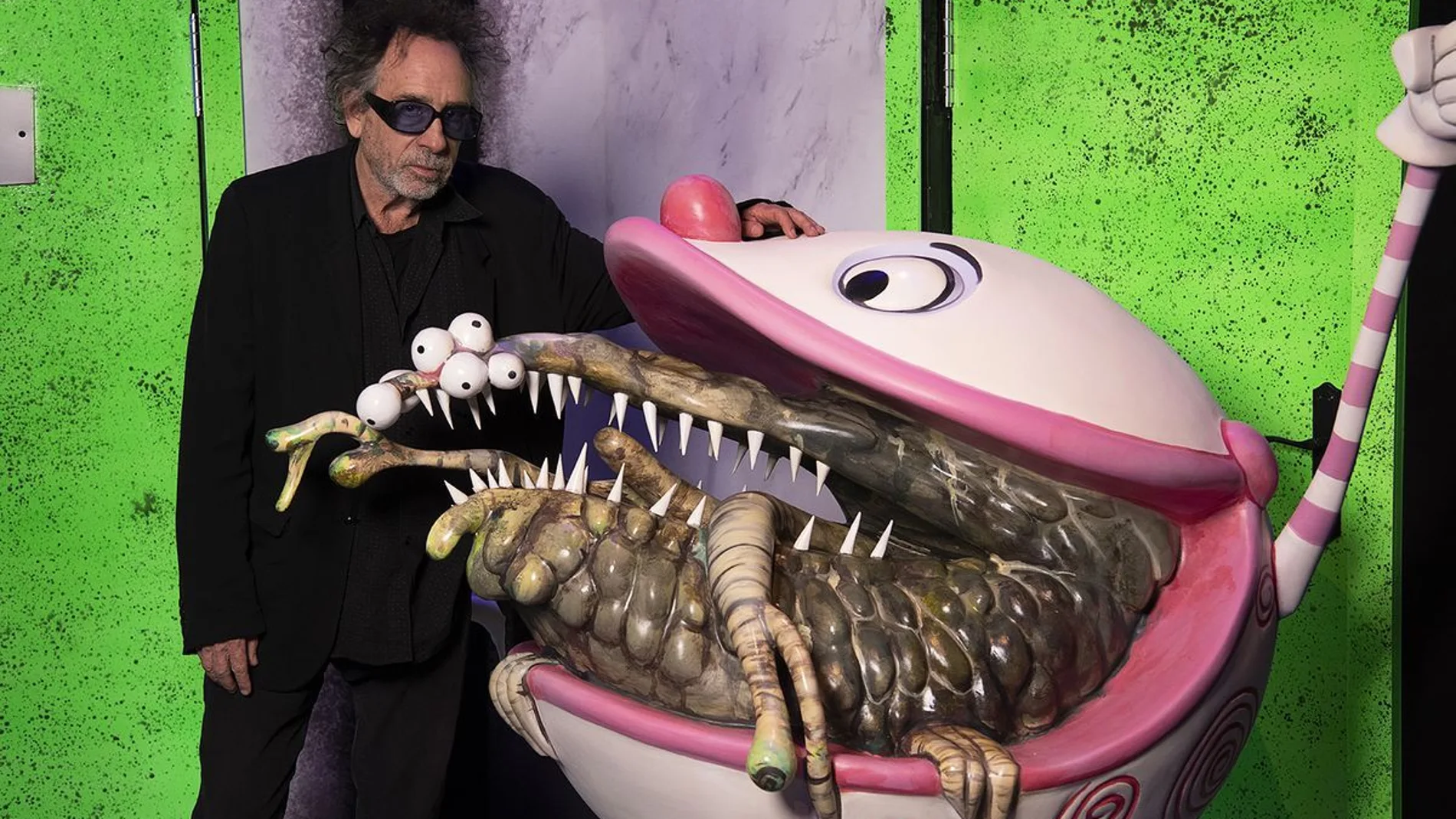 El cineasta Tim Burton posa junto a uno de sus bocetos exclusivos e inéditos presentes en la exposición
