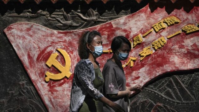 Mujeres con mascarilla pasan por un mural del partido comunista en Pekín, China