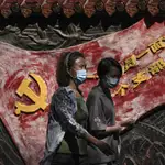 Mujeres con mascarilla pasan por un mural del partido comunista en Pekín, China