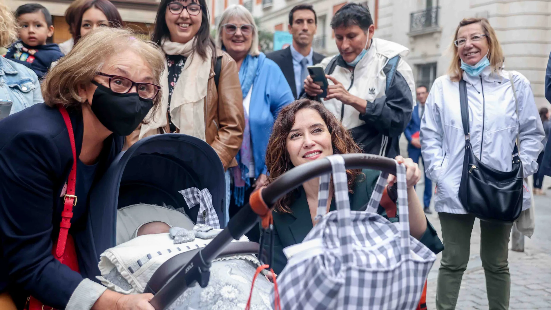 La presidenta de la Comunidad de Madrid, Isabel Díaz Ayuso, se toma una fotografía con una mujer y un bebé a su llegada a la Real Casa de Correos para visitar una muestra de los sistemas y dispositivos tecnológicos implantados en la red de transporte público