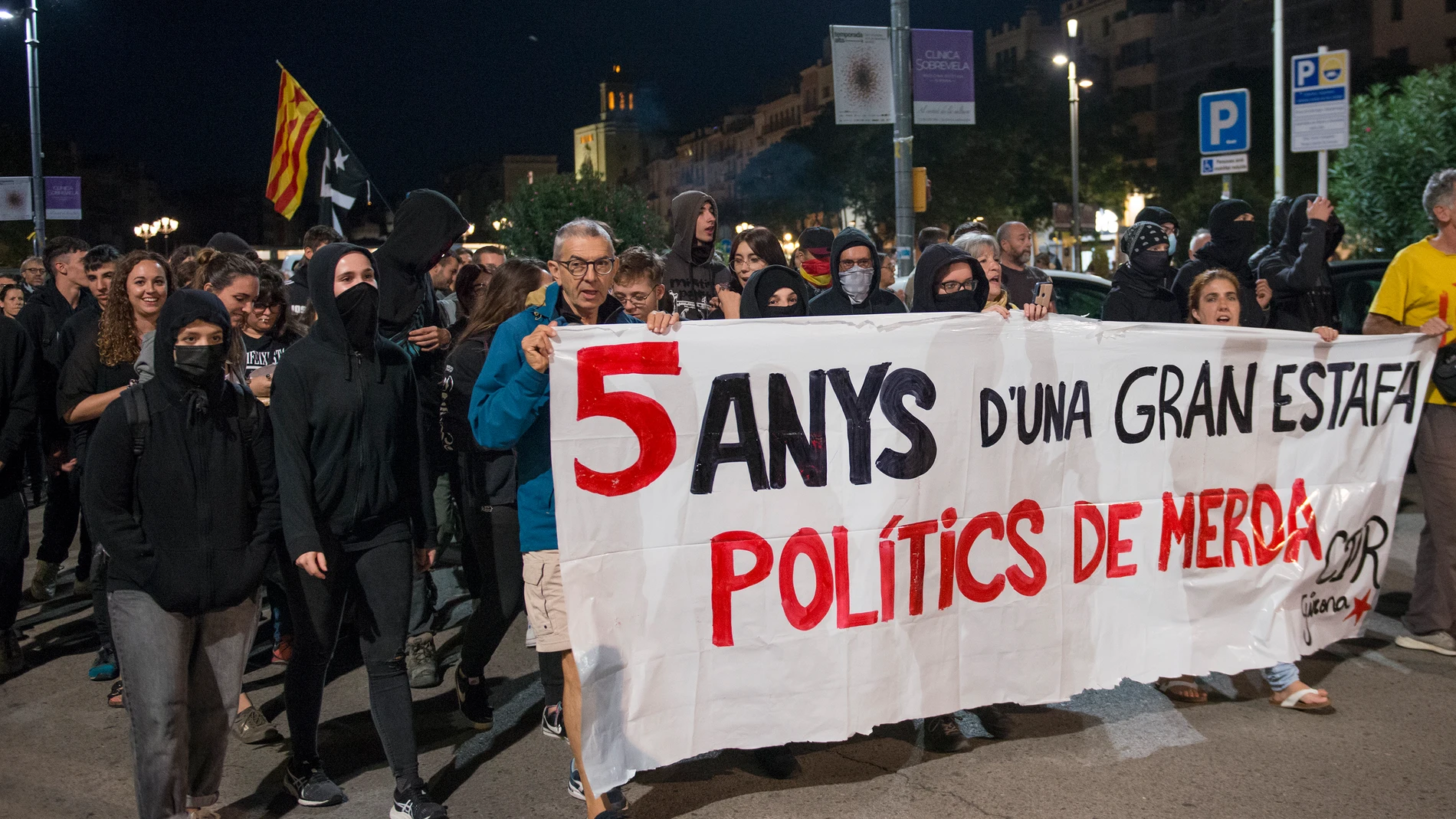 Miembros del CDR Girona portan una pancarta que dice "cinco años de una gran estafa. Políticos de mierda" durante una manifestación con motivo del quinto aniversario del referéndum del 1-O.