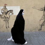 Una mujer iraní con velo pasa junto a una pared dibujada en Teherán