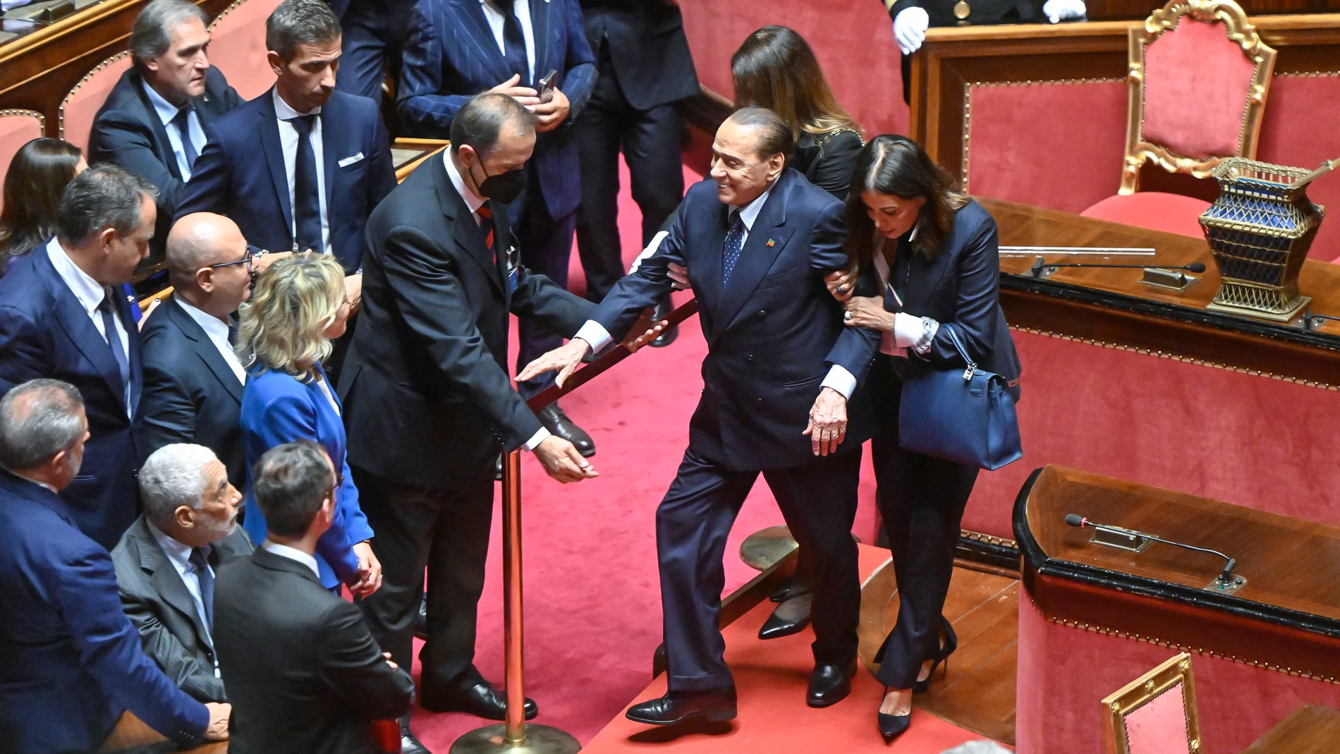 Los ujieres del Senado italiano ayudan ayer a Silvio Berlusconi a llegar a su escaño, en la Cámara Alta