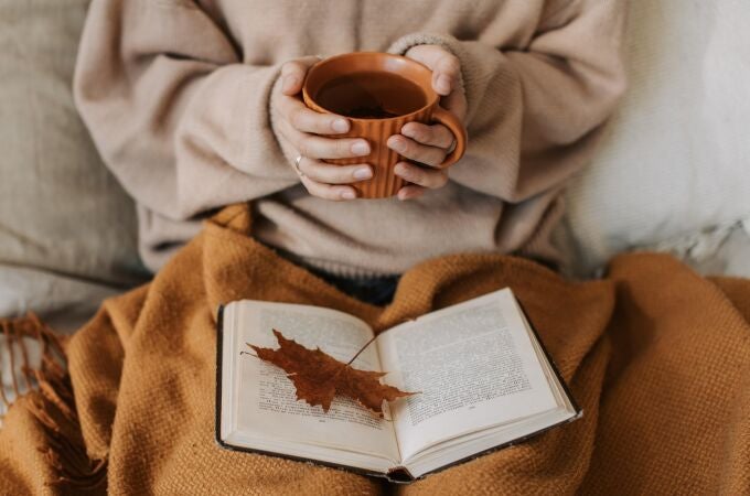Mujer leyendo un libro con una taza de té en al mano