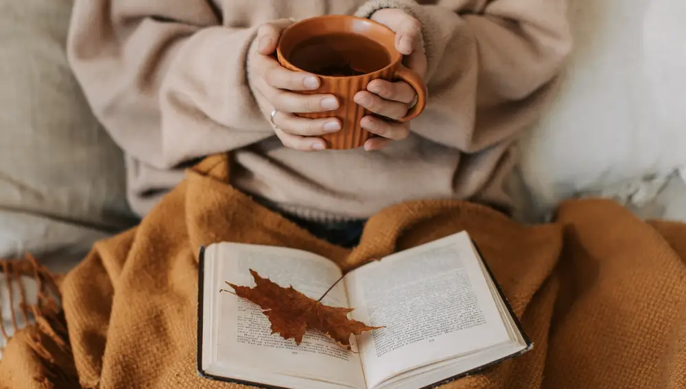 Mujer leyendo un libro con una taza de té en al mano