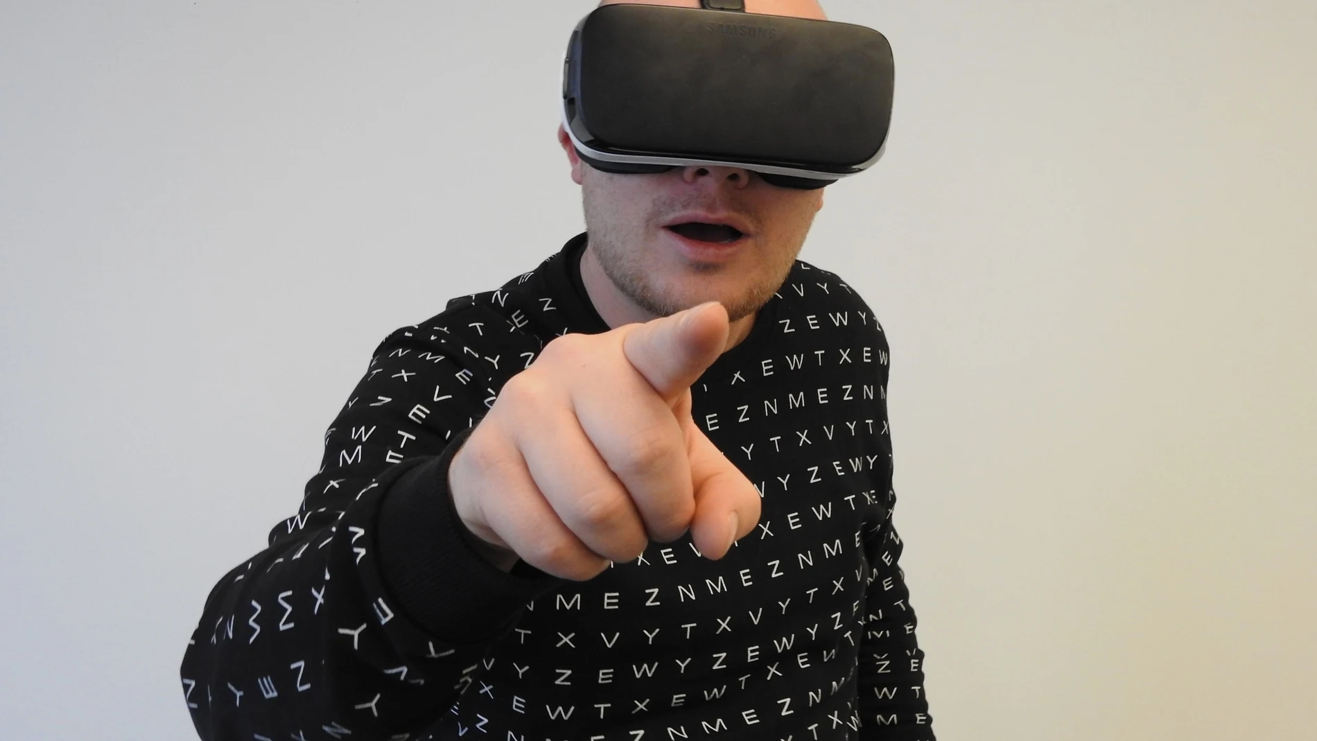 Un hombre con un casco de realidad virtual y gesto sorprendido, señalando hacia la cámara con el dedo índice
