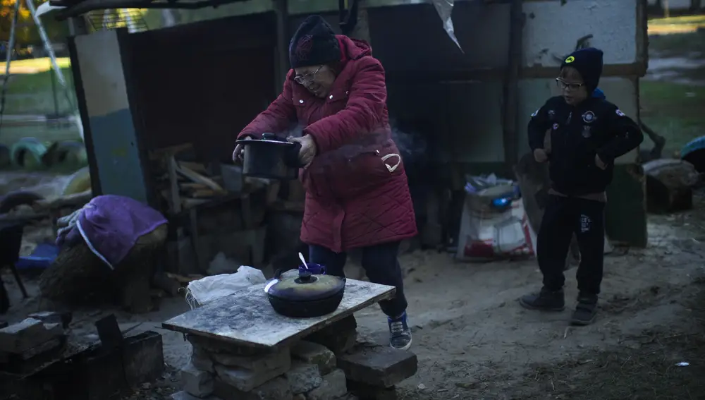 Iryna Panchenko saca una olla de comida de una estufa improvisada junto a su nieto Artem en Kivsharivka