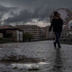Una mujer se refugia de la lluvia con un paraguas mientras camina por el puente romano de Ourense