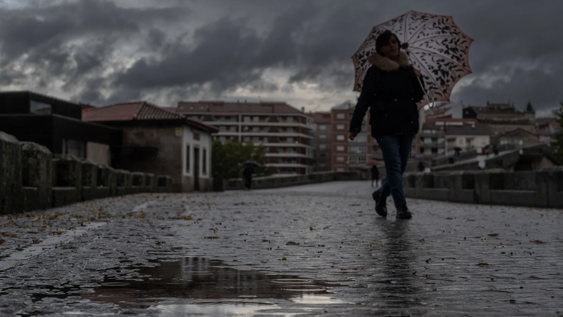 Una mujer se refugia de la lluvia con un paraguas mientras camina por el puente romano de Ourense