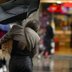 Una mujer con un perro intenta controlar y protegerse con un paraguas