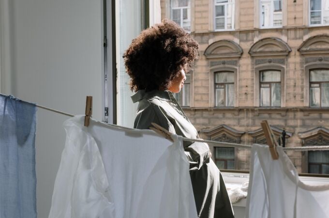 Mujer mirando por la ventana junto a ropa tendida