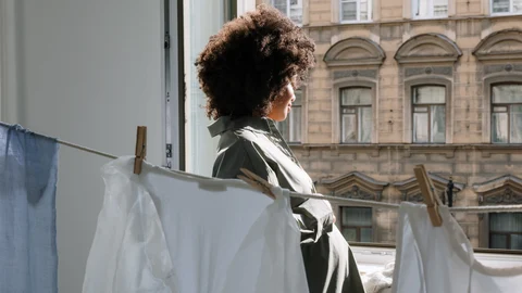 Mujer mirando por la ventana junto a ropa tendida