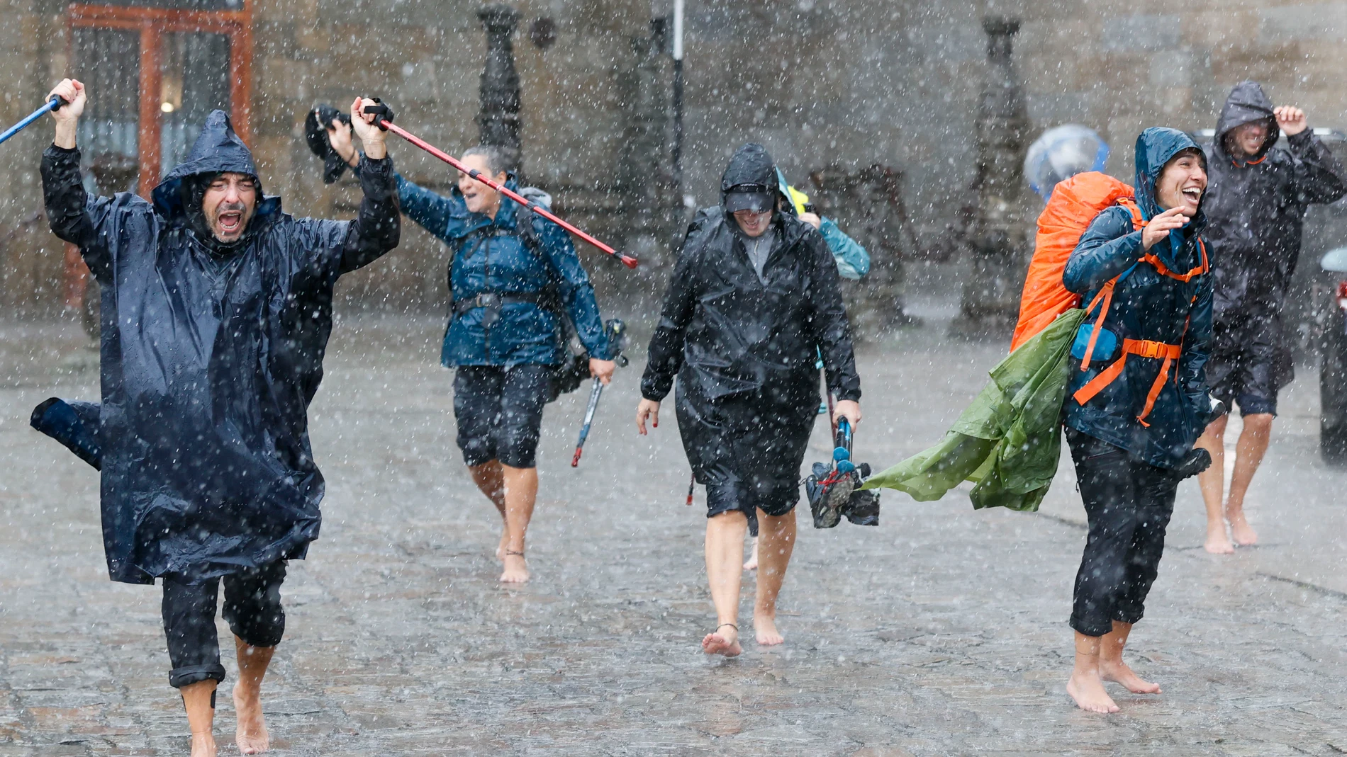 Un grupo de peregrinos termina el Camino de Santiago bajo un chubasco en el plaza del Obradoiro, en Santiago de Compostela