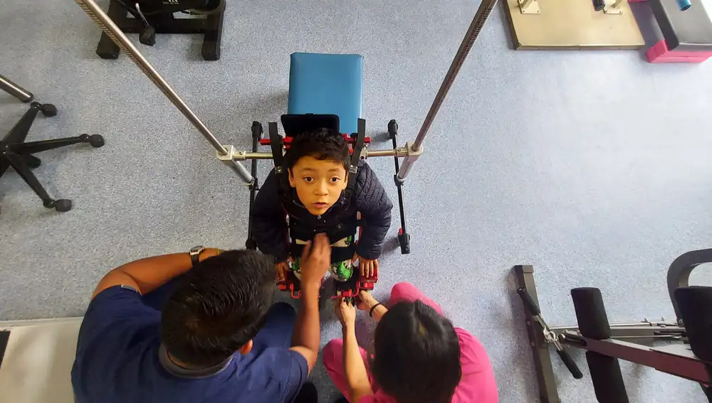 Fernando espera a que le ajusten las cuerdas para poder levantarse, andar y jugar con el exoesqueleto Atlas 2030. Su madre explica que este robot supone “enormes expectativas de mejora” para tratar su parálisis cerebral.